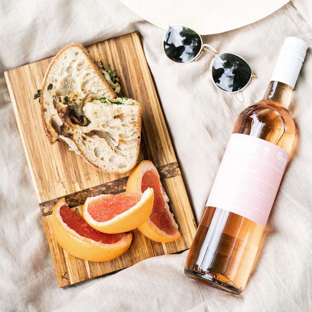Bottle of rosé wine, sliced bread, and grapefruit on a wooden board with sunglasses.